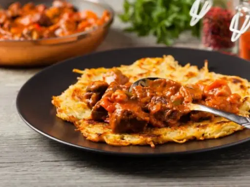 Gęsty, aromatyczny sos do placków ziemniaczanych z kawałkami mięsa i warzyw, podany na chrupiących plackach.