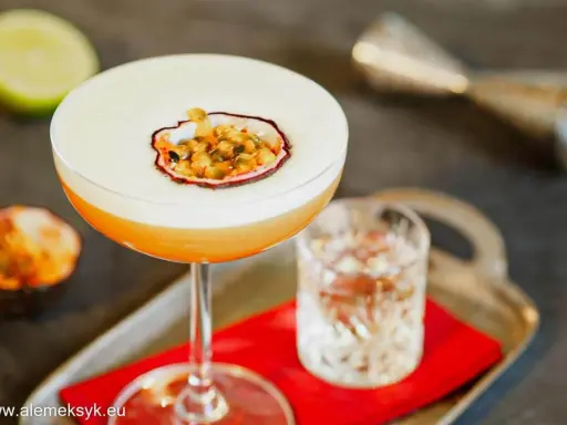 Pyszny drink Pornstar Martini z pianką i owocem marakui, obok kieliszek z drinkiem i połówka limonki.