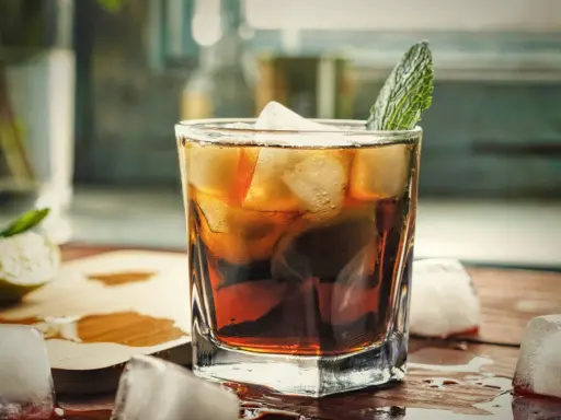 Orzeźwiający gin z colą, z lodem i listkiem mięty, na drewnianym blacie. Idealny na letnie popołudnie.