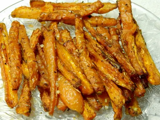 Chrupiące, pieczone frytki z marchewki, przyprawione ziołami i czosnkiem, podane na szklanej tacy.