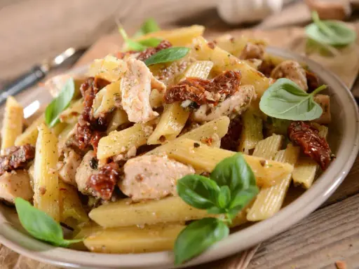 Penne z kurczakiem i suszonymi pomidorami, udekorowane świeżą bazylią. Pyszne danie na obiad.