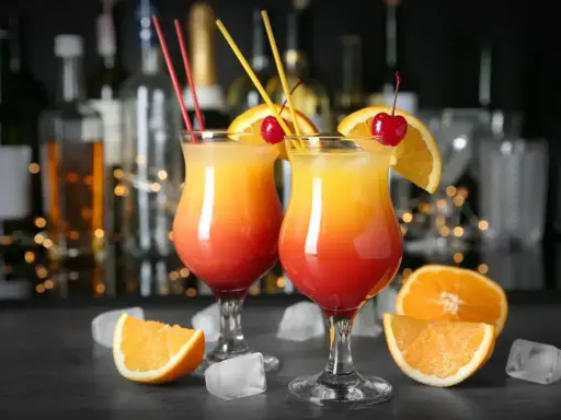 Dwa drinki z wódką, ozdobione pomarańczą i wiśnią, na tle barowych butelek. Idealne na letnie wieczory.