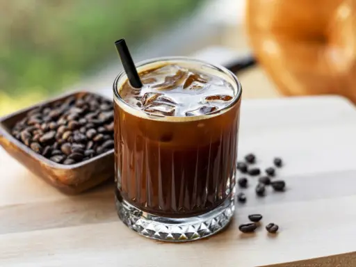 Orzeźwiający cold brew z lodem i słomką, obok miseczka z ziarnami kawy. Idealny na gorący dzień.