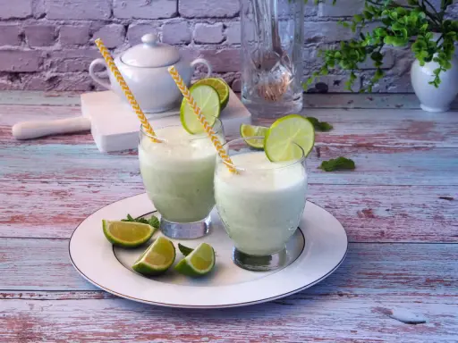 Dwa orzeźwiające drinki z mlekiem skondensowanym, ozdobione plasterkami limonki i miętą, na talerzu.