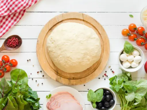 Świeże ciasto na pizzę, pomidorki, mozzarella, oliwki i szynka. Zastanawiasz się, ile może leżeć ciasto na pizzę w lodówce?