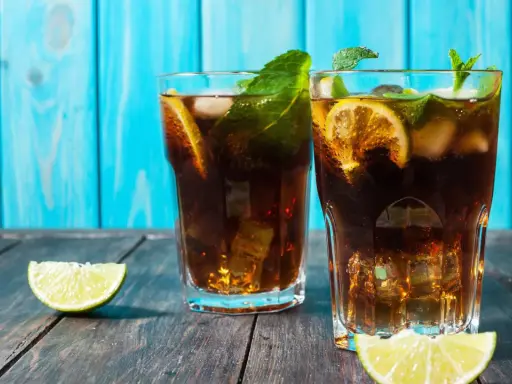Dwa orzeźwiające drinki z rumem ciemnym, lodem, cytryną i miętą na drewnianym blacie.