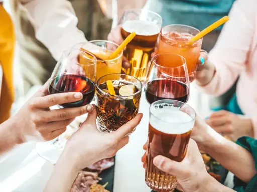 Ręce wznoszą kieliszki z winem, drinkami i piwem, celebrując wspólne chwile.