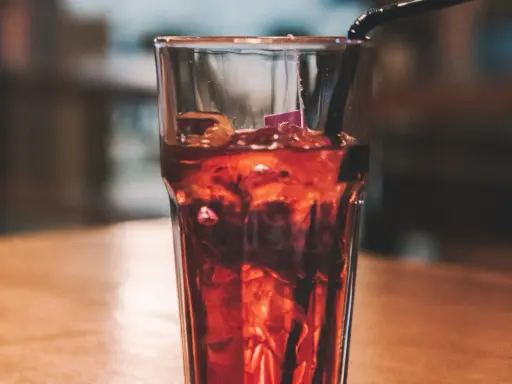 Szklanka z lodem i ciemnym napojem, idealne proporcje whisky z colą. Czarna słomka zanurzona w napoju.