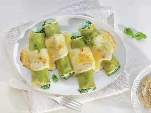Zielone cannelloni ze szpinakiem, polane kremowym sosem i zapieczone z serem. Pyszne danie gotowe do podania.