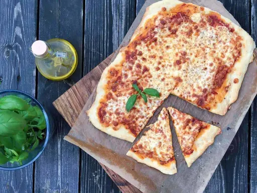 Pyszna pizza margherita z roztopionym serem i świeżą bazylią, obok butelka oliwy i miseczka ziół.