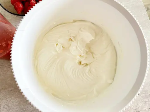 Gładki, puszysty krem z mascarpone w białej misie, gotowy do deseru. Obok miski widać miseczkę z truskawkami.