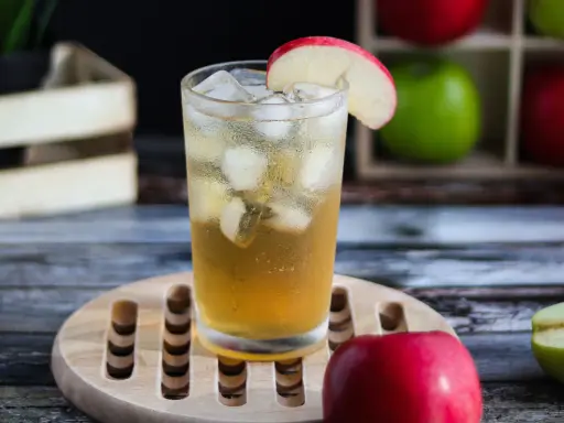 Orzeźwiający drink z sokiem jabłkowym, lodem i plasterkiem jabłka. W tle skrzynka z jabłkami.