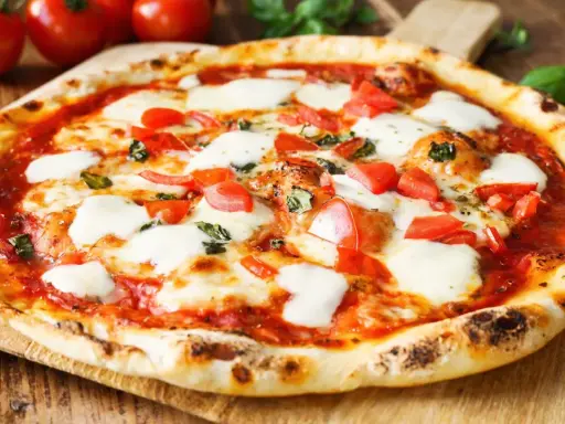 Pyszne ciasto na pizzę bez wyrastania, z pomidorami i mozzarellą, na drewnianej desce.