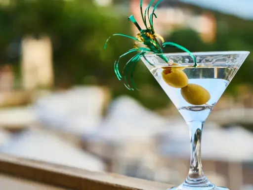 Orzeźwiający martini fiero drink z oliwkami, ozdobiony zieloną wstążką, na tle rozmytego, letniego krajobrazu.