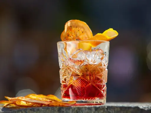 Klasyczny whisky old fashioned w kryształowej szklance, ozdobiony skórką pomarańczy i suszonym owocem.
