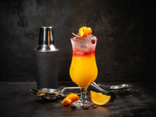 Kolorowy drink Sex on the Beach z pomarańczą i żurawiną, obok shakera i akcesoriów barmańskich. Idealny przepis na lato!