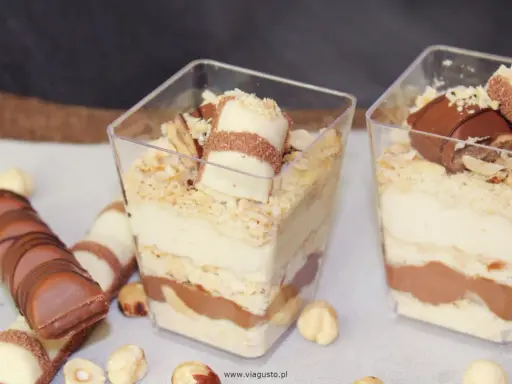 Pyszne ciasto Kinder Bueno w pucharkach, przełożone kremem i czekoladą, posypane orzechami.