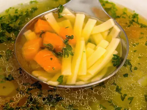Łyżka nabiera aromatyczny bulion warzywny z marchewką i makaronem nitki.