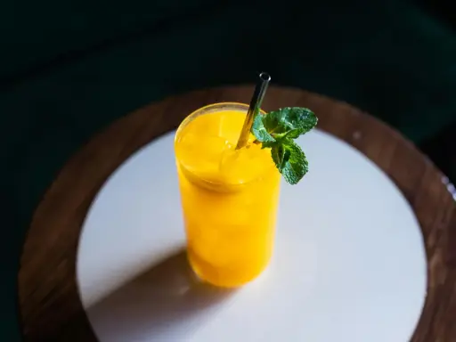 Orzeźwiający drink z mango, z kostkami lodu i listkiem mięty, podany w szklance ze słomką.