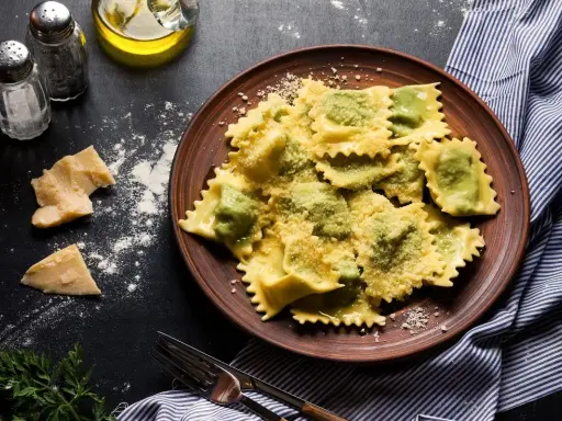 Pyszne ravioli z ricottą i szpinakiem, posypane parmezanem, na brązowym talerzu. Obok kawałki sera i przyprawy.