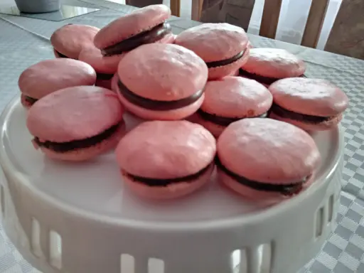 Różowe makaroniki na bezie włoskiej z czekoladowym nadzieniem, ułożone na białej paterze.