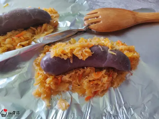 Kaszanka z grilla z kapustą kiszoną, gotowa do podania. Obok drewniany widelec.