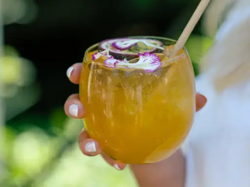 Orzeźwiający drink z marakują, ozdobiony kwiatami i plasterkiem owocu. Idealny na upalne dni.