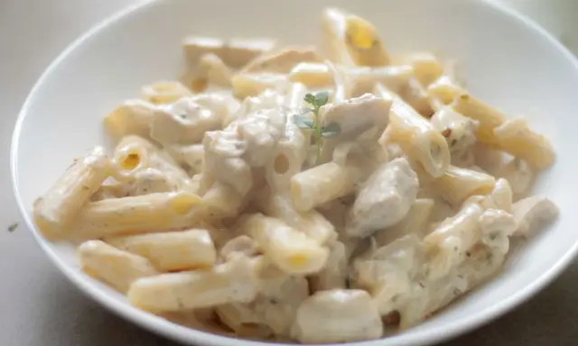 Penne z kurczakiem w kremowym sosie, udekorowane gałązką ziół. Pyszne danie, które zachwyci każdego smakosza.
