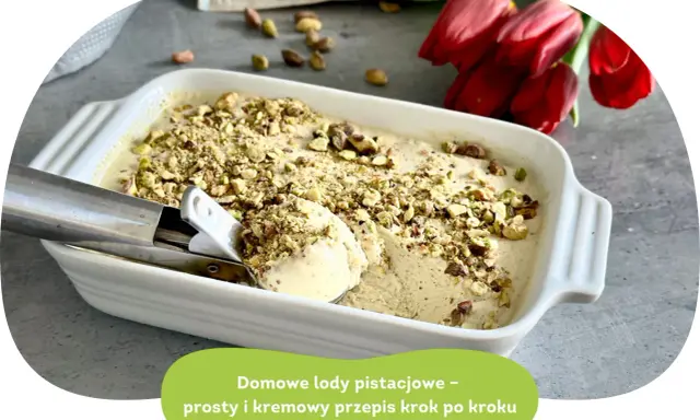 Kremowe lody pistacjowe w białej formie, posypane orzechami. Łyżka właśnie nabiera porcję tego pysznego deseru.