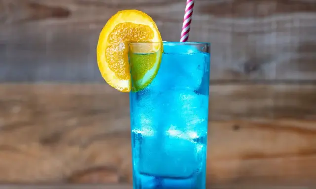 Orzeźwiający drink z blue curacao, ozdobiony plasterkiem pomarańczy i limonki, z kolorową słomką. Idealny na letnie popołudnie.