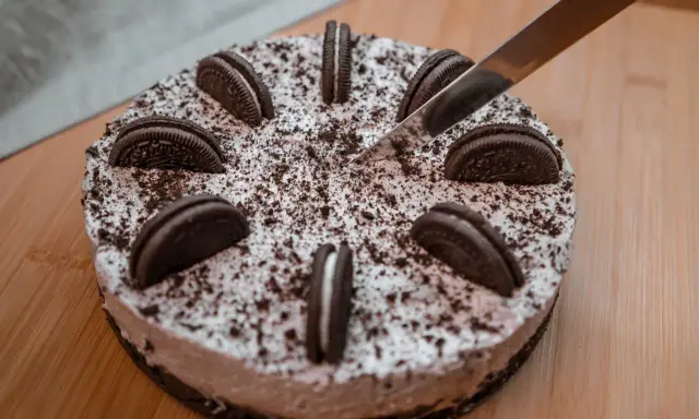 Pyszny sernik oreo, ozdobiony ciasteczkami i posypką, czeka na pokrojenie.