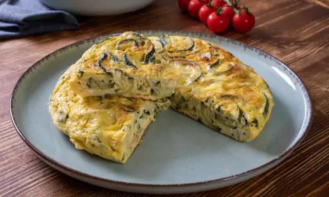 Pyszna frittata z cukinią, podana na talerzu, z pomidorkami koktajlowymi w tle.