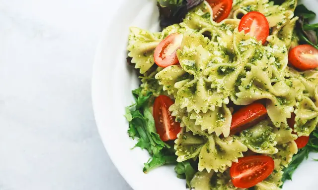 Makaron farfalle z zielonym pesto ze słoika, udekorowany połówkami pomidorków koktajlowych i listkami sałaty.