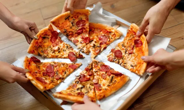 Ręce sięgają po kawałki pysznego ciasta na pizzę z kiełbasą i grzybami.