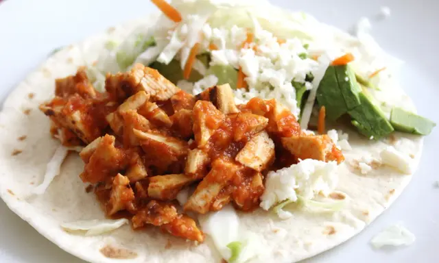 Pyszna tortilla z kurczakiem w sosie, posypana serem feta, z dodatkiem świeżej sałaty i awokado.