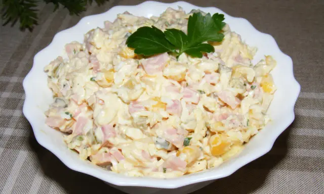 Pyszna sałatka z szynką, jajkiem, kukurydzą i ogórkiem, udekorowana natką pietruszki. Idealna na każdą okazję.