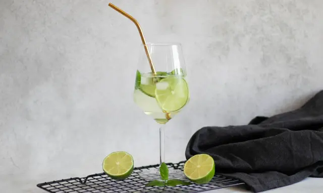 Orzeźwiający drink Hugo z limonką i miętą, idealne proporcje na lato. Złota słomka dodaje elegancji.