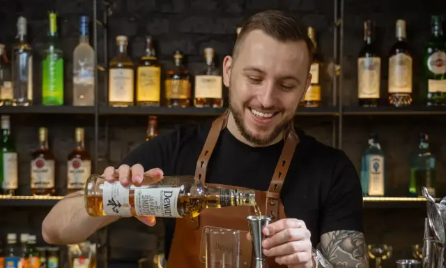 Uśmiechnięty barman, który robi drinki, nalewa whisky Dewar's do jiggera.
