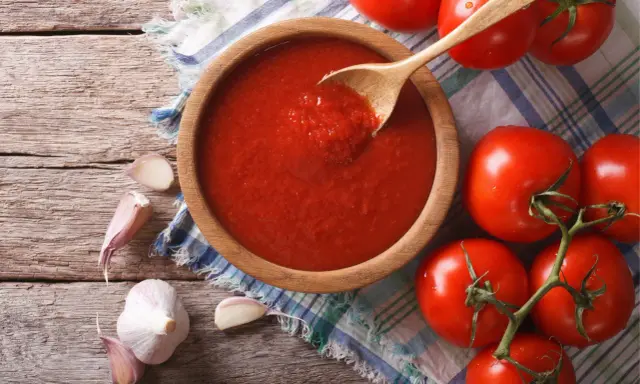 Domowy sos do pizzy z koncentratu, czosnek i świeże pomidory na drewnianym blacie.