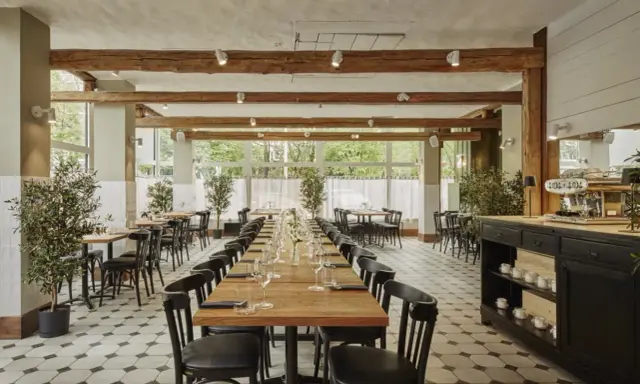 Elegancka sala restauracyjna z długimi stołami, idealna na degustację **primitivo kuchnia i wino**. Drewniane belki i duże okna tworzą przytulną atmosferę.