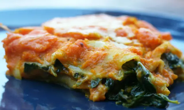 Pyszne lasagne ze szpinakiem, z pomarańczowym sosem i ciągnącym się serem, na granatowym talerzu.