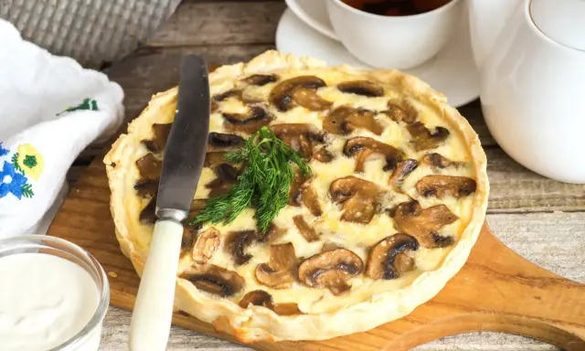 Pyszna tarta z pieczarkami, podana z kubkiem herbaty i śmietaną. Idealna na jesienny obiad.