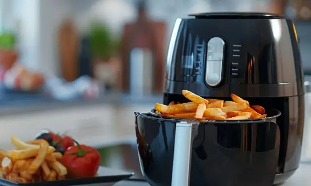 Frytki z frytkownicy beztłuszczowej, idealne do wypróbowania nowych air fryer przepisy. Obok talerz z frytkami, pomidorkami i oliwkami.