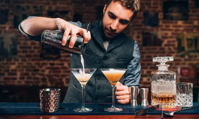 Barman przygotowuje drinki, zastanawiając się, jaki rum do mojito będzie najlepszy. Na blacie stoją kieliszki i karafka z bursztynowym płynem.