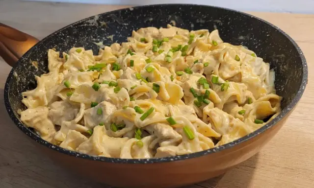 Tagliatelle z kurczakiem w sosie śmietanowym, posypane szczypiorkiem, podane w patelni. Pyszne danie gotowe do spożycia.