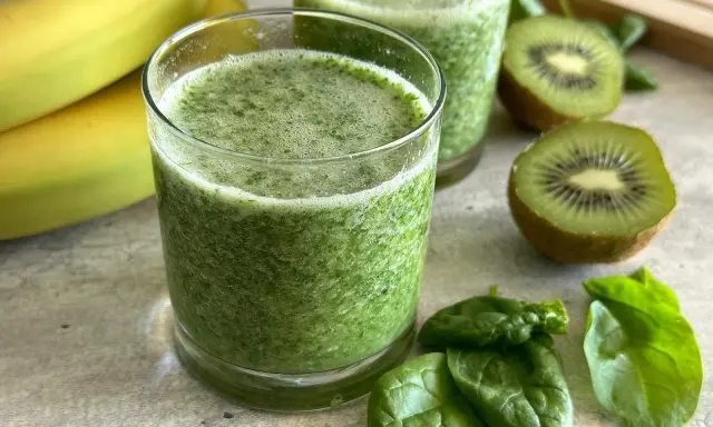 Orzeźwiający koktajl ze szpinakiem, bananami i kiwi. Zielony napój w szklance, obok świeże liście szpinaku i owoce.