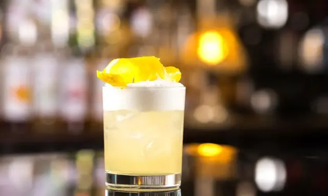 Klasyczny whisky sour z pianką i skórką cytryny, idealny na wieczór.