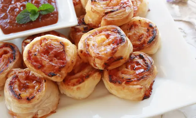 Pyszne przekąski na andrzejki: zawijane roladki z ciasta francuskiego z nadzieniem, podane z sosem.