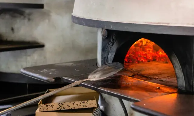 Piec do pizzy z rozżarzonymi węglami. Łopatka czeka, by włożyć do środka pizzę, która będzie piec się w 200 stopniach.