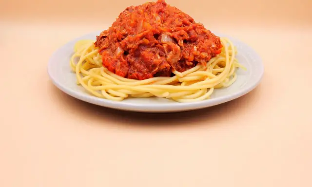Porcja spaghetti z sosem pomidorowym i tuńczykiem, podana na jasnym talerzu.